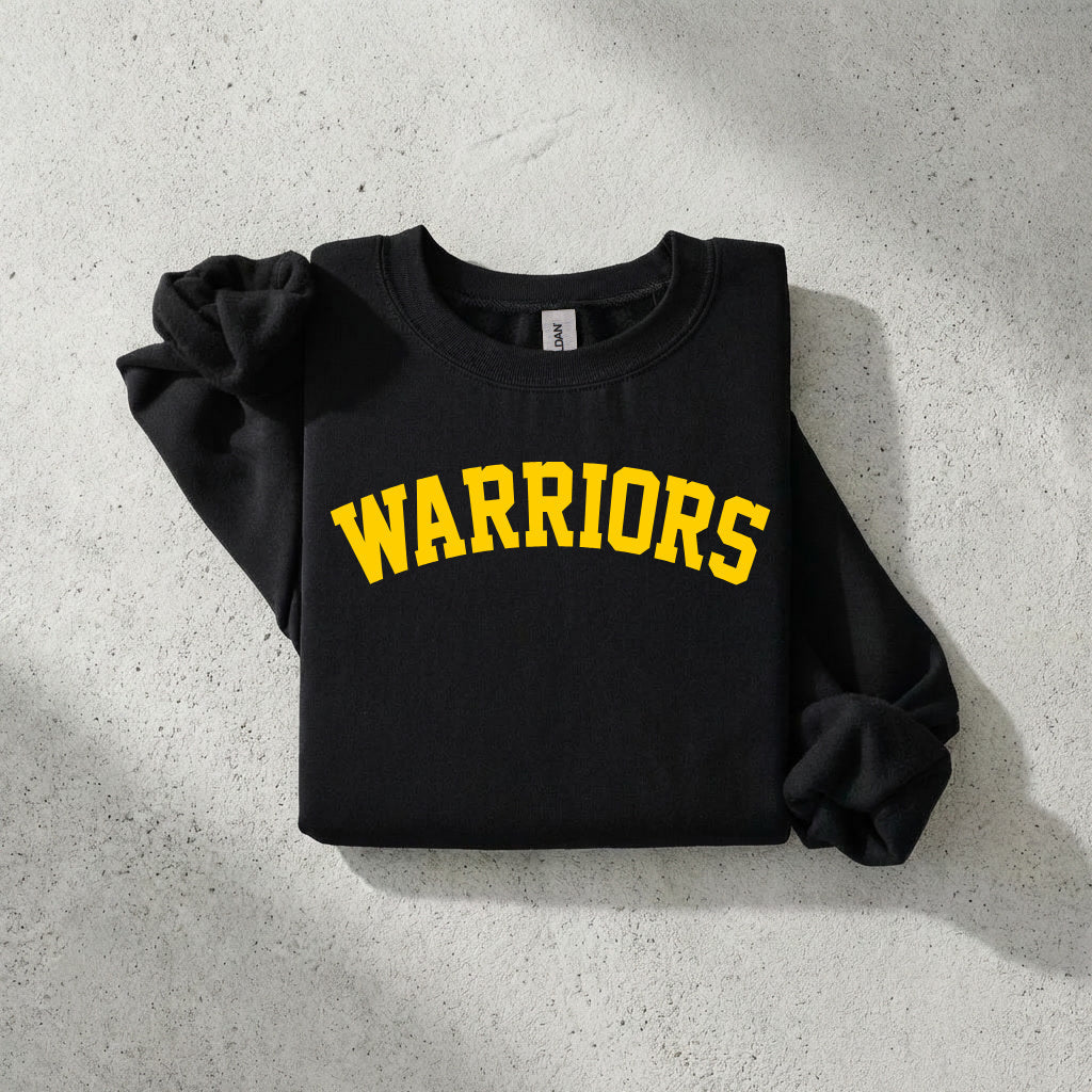 A black crewneck sweatshirt with 'WARRIORS' printed in yellow arched block letters across the chest, styled flat on a textured gray concrete surface.